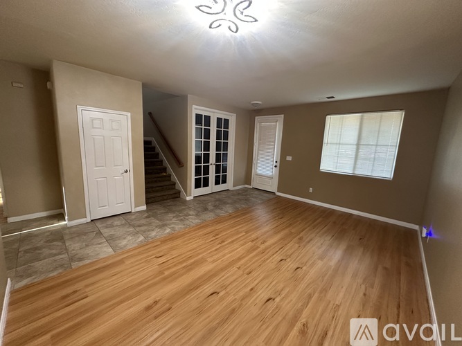 A room with wooden flooring and a staircase in the background.