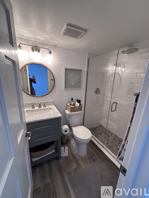 A bathroom with a toilet, sink, mirror, and shower.