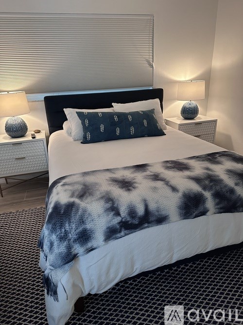 A bed with a blue and white patterned comforter is in the foreground of a room with two lamps on bedside tables.