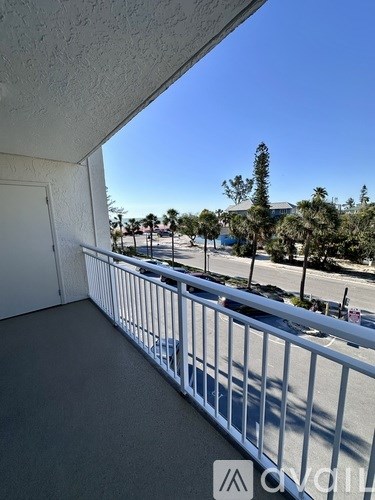 A balcony with a white railing overlooks a parking lot and palm trees.