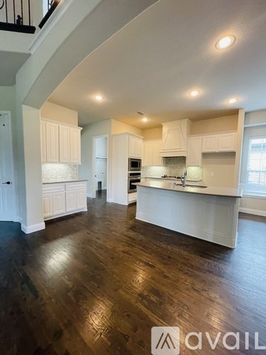 A spacious kitchen with white cabinets and a dark hardwood floor.