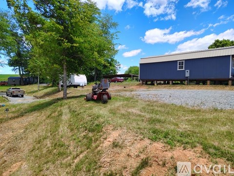 A blue building sits in a field with a tractor and a car in the background.