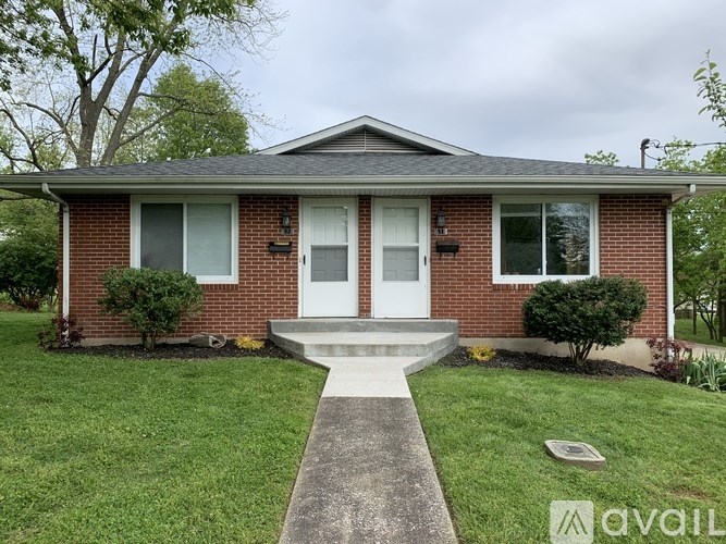 A brick house with a white door and a concrete walkway leading to it.