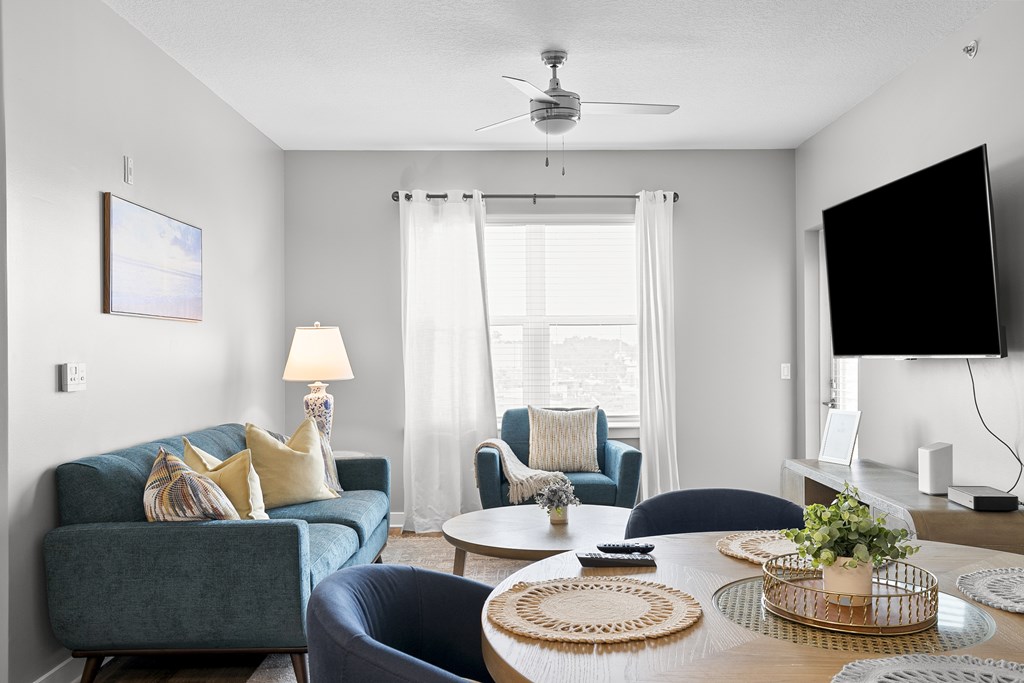A living room with a blue couch, a white table, and a flat screen TV mounted on the wall.