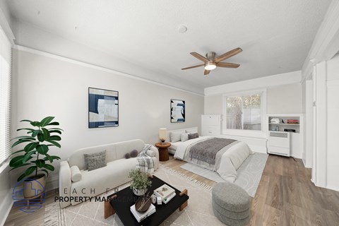 A well-lit, spacious living room with a white sofa, a grey ottoman, and a coffee table.
