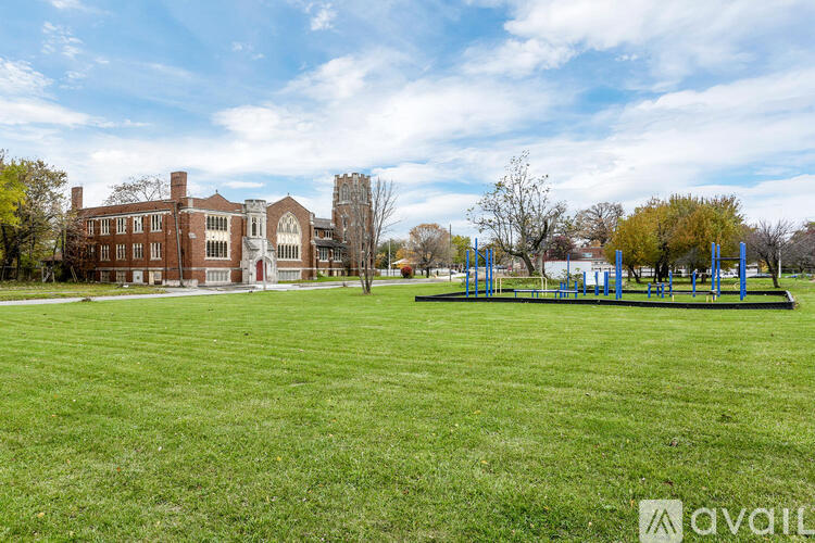 A large grassy field with a playground and a red brick building in the background.