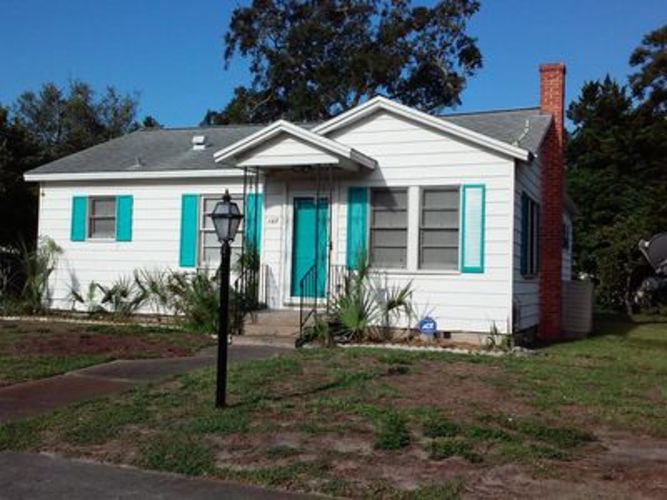 A white house with a red brick chimney and turquoise shutters.