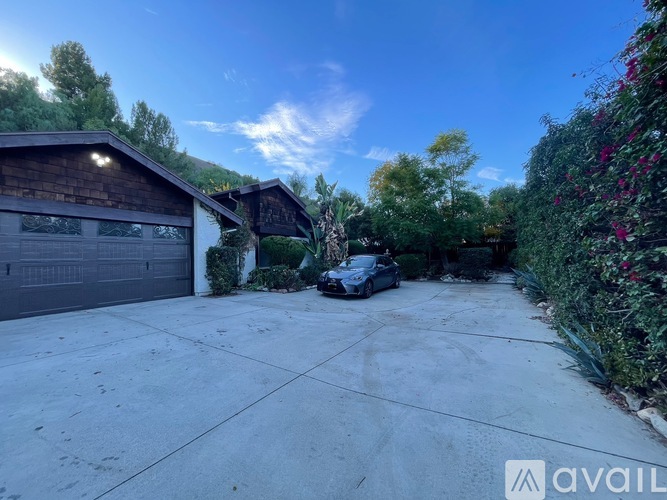 A car is parked in a driveway with a garage and trees in the background.