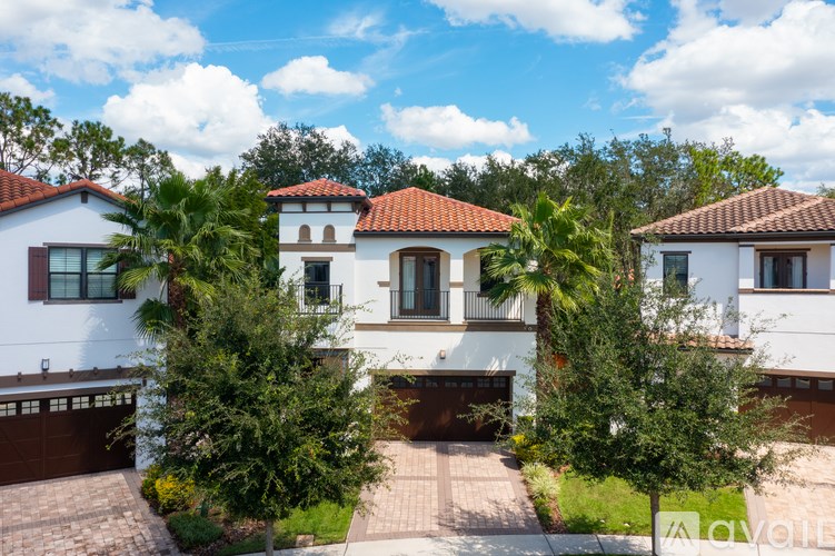 A white house with a red tile roof is surrounded by trees.