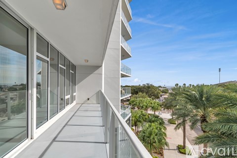 A balcony with glass doors overlooks a palm tree lined street.