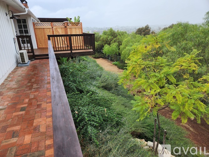 A balcony with a red brick floor and a wooden railing overlooks a garden.