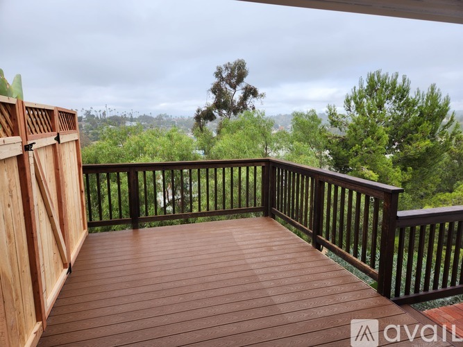 A wooden deck with a railing and a view of the trees and sky.