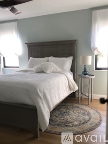 A bedroom with a bed, a small table with a lamp, and a rug on the floor.