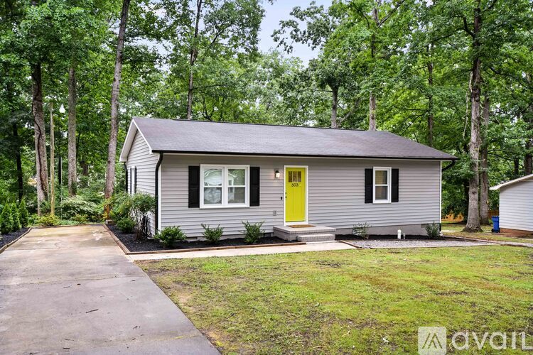 A small house with a yellow door is surrounded by greenery.