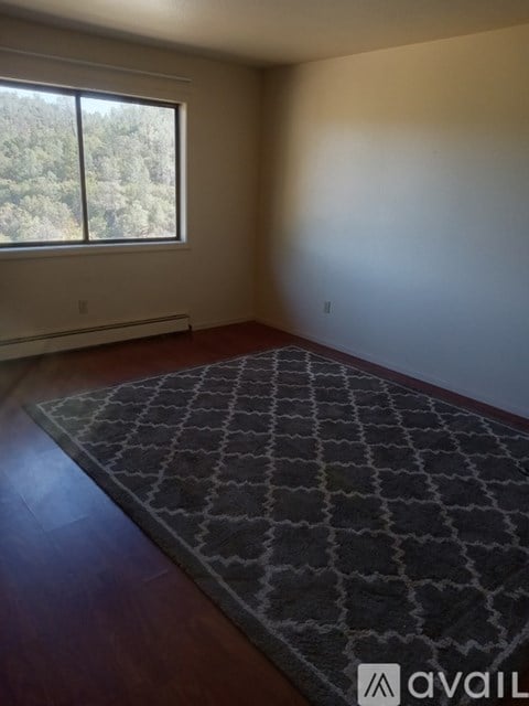 A room with a rug and a window overlooking trees.