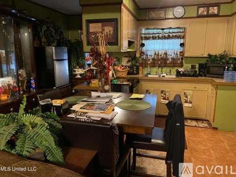 A kitchen with a table and chairs in the foreground and a refrigerator, microwave, and oven in the background.