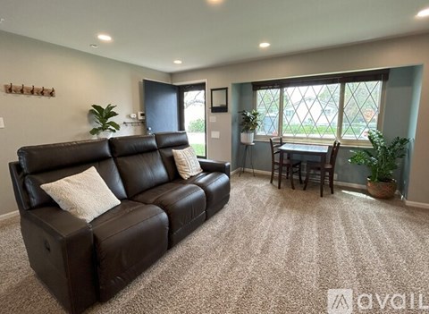 A living room with a black leather couch and a dining table with chairs.