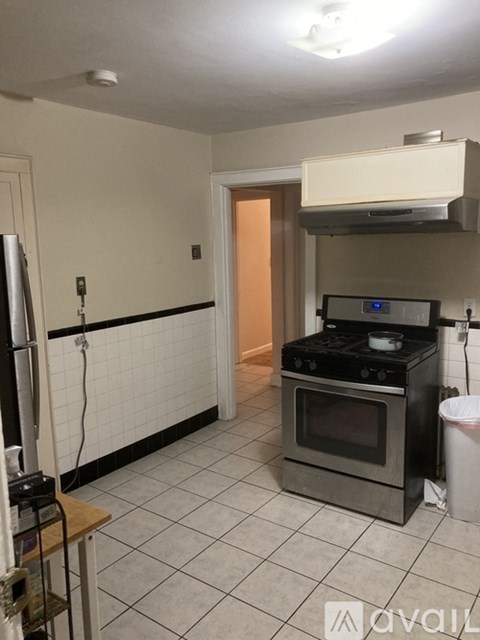 A kitchen with a stove and oven, a refrigerator, and a trash can.