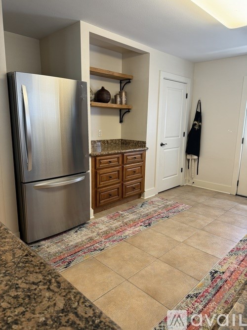 A kitchen with a refrigerator and a rug on the floor.