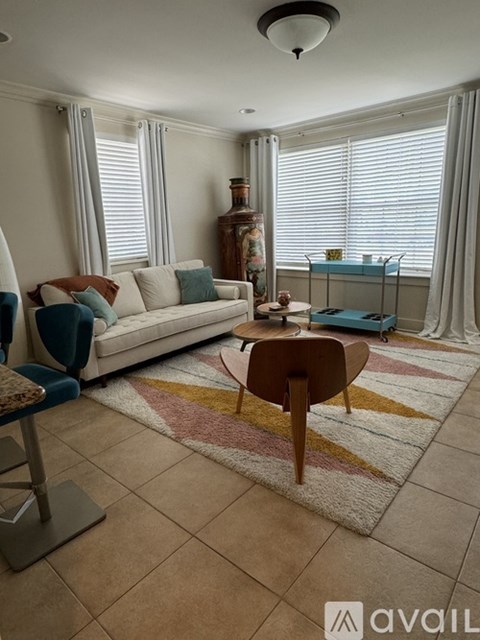 A living room with a white couch, a wooden chair, and a rug with a multicolored pattern.