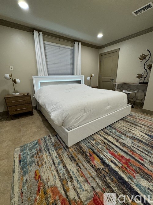 A bedroom with a large bed, a wooden nightstand, and a colorful rug.