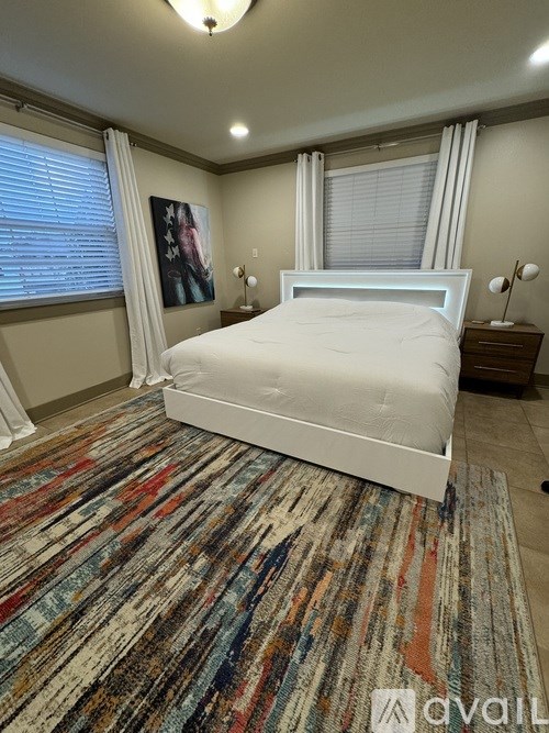 A bedroom with a white bed and a multicolored rug.