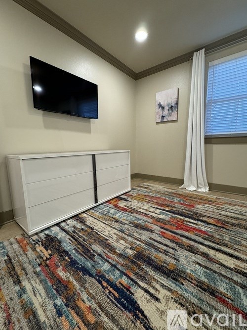 A room with a white dresser and a flat screen TV mounted on the wall.