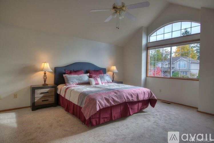 A bedroom with a bed, two lamps, and a ceiling fan.
