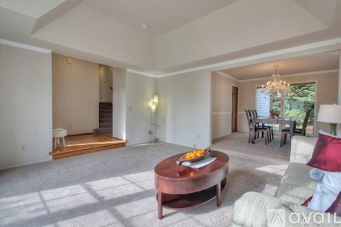 A living room with a coffee table in the center and a dining area in the background.