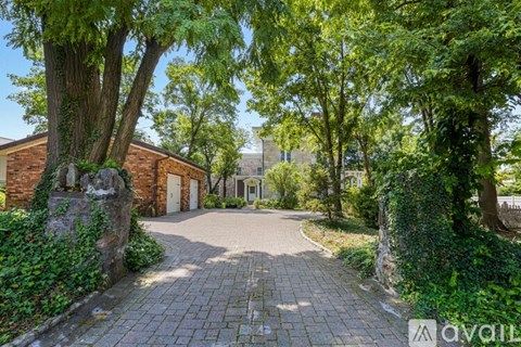 A driveway leads to a house with a stone wall on one side and trees on the other.