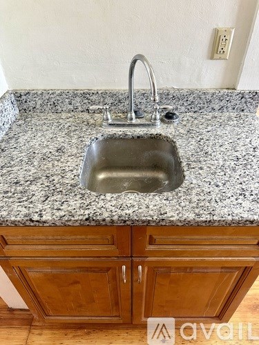 A kitchen sink with granite countertop and wooden cabinets.