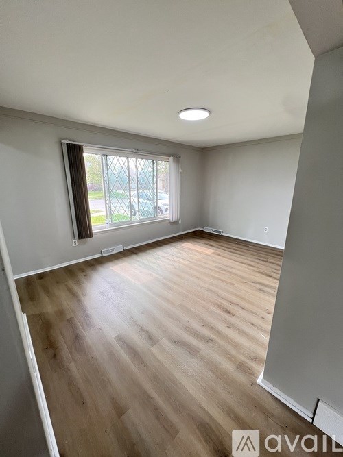 A room with wooden flooring and a window with a view of a fence and trees outside.