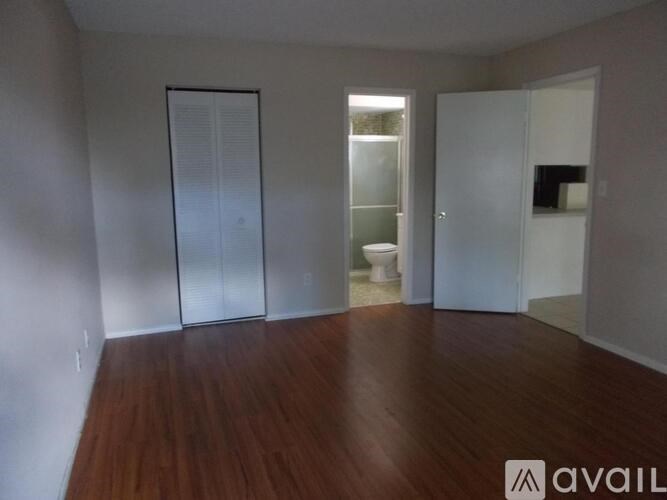 A room with wooden floors and white walls, with a glass door leading to a bathroom.