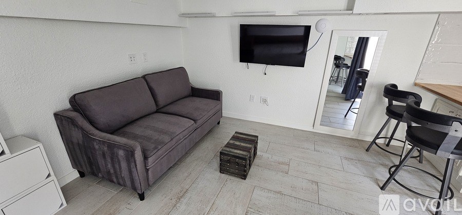 A grey couch sits in a living room with a television mounted on the wall.
