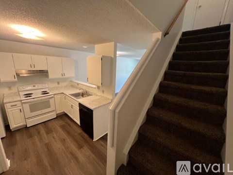 A kitchen with white cabinets and a staircase with a brown carpet.