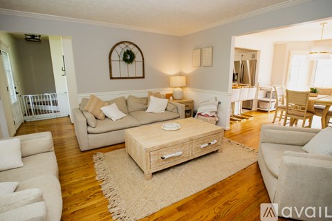 A living room with a white couch, a coffee table, and a baby crib in the background.