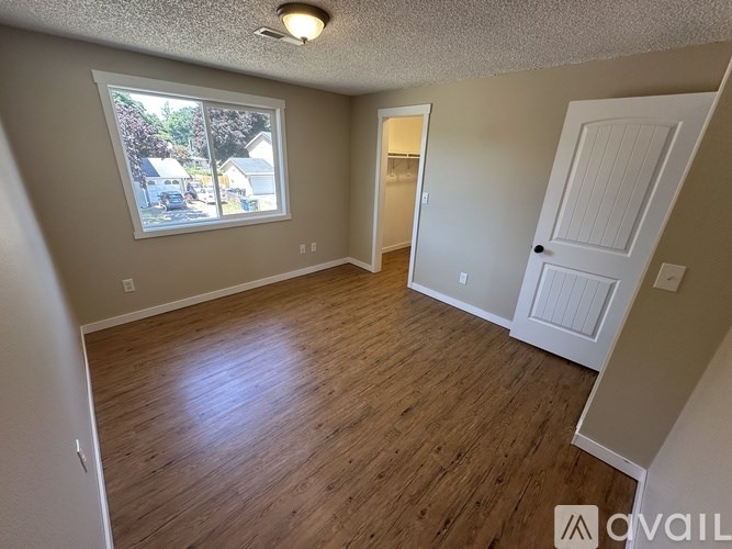 A room with wooden floors and a window showing a view of houses.