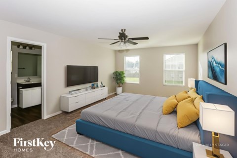 A bedroom with a bed, a television, a ceiling fan, and a lamp.