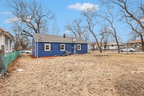 A blue house with a white fence and bare trees in the background.