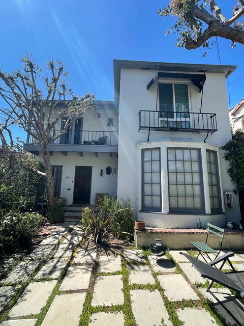 A white house with a balcony and a tree in front.