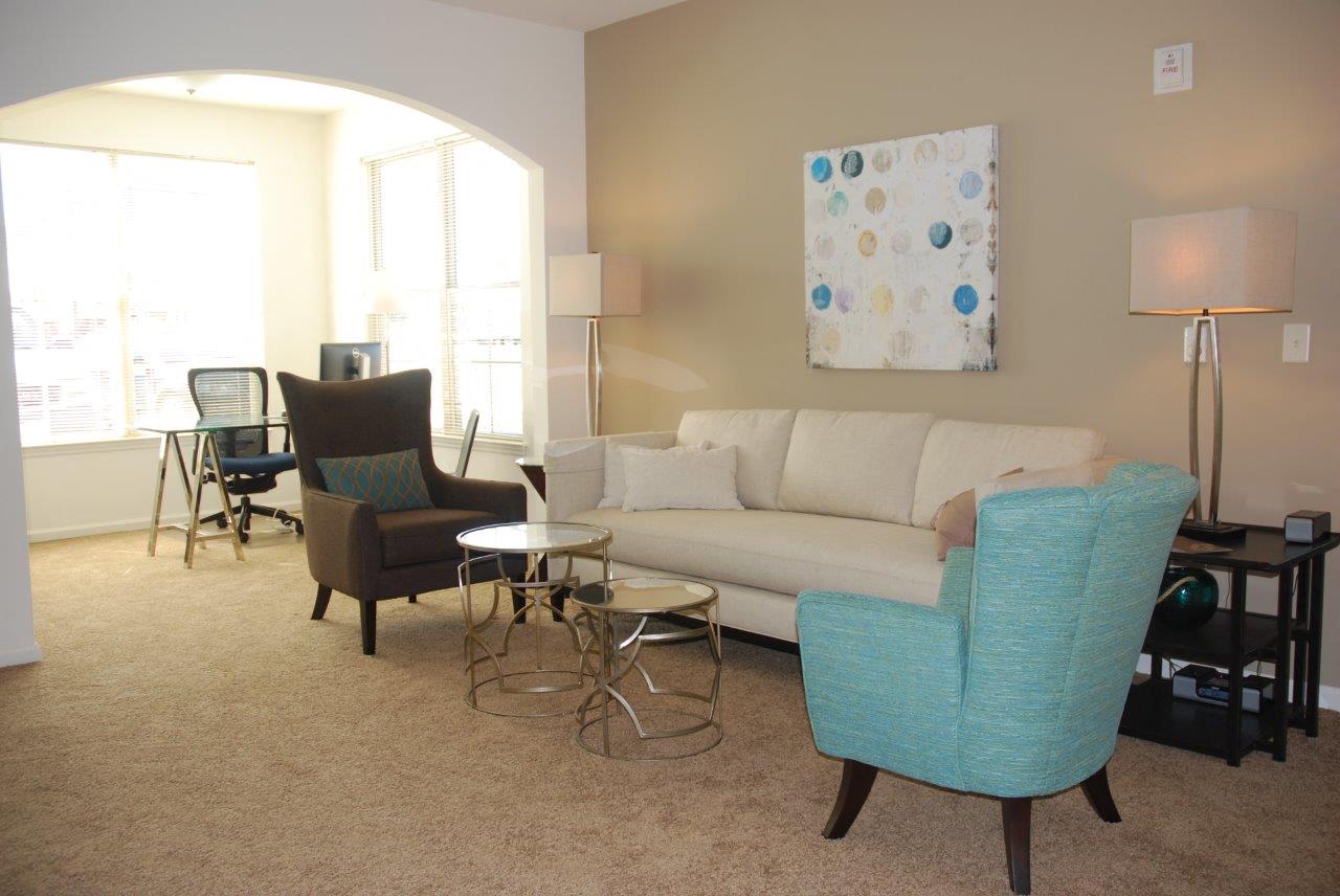 A living room with a white couch, a blue chair, and a painting on the wall.