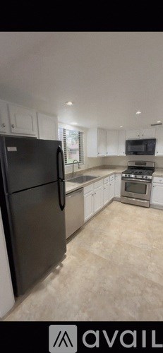 A black refrigerator stands in a kitchen with white cabinets and a tiled floor.
