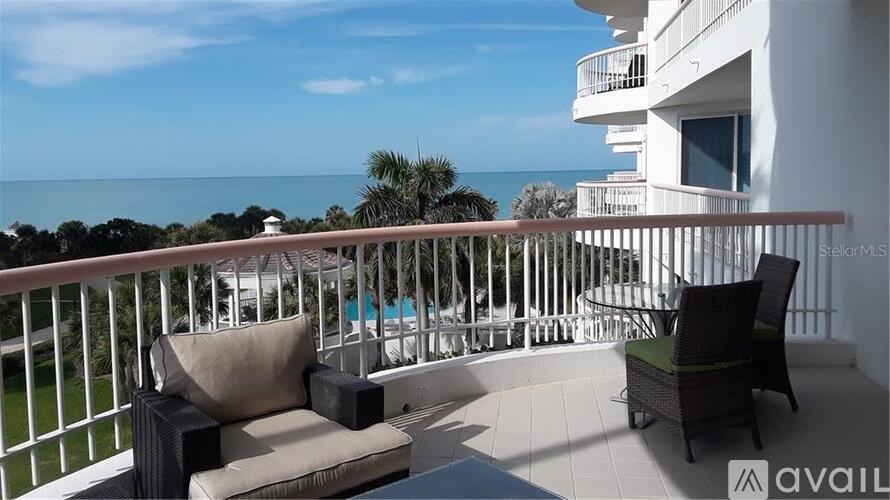 A balcony with a couch and chairs overlooking the ocean.