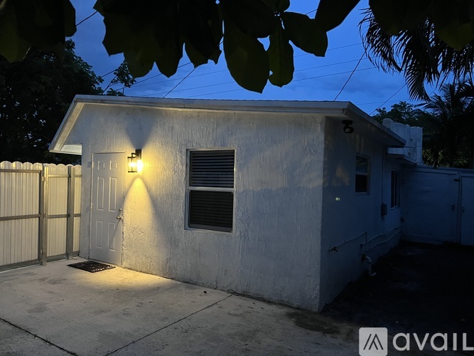 A small white house with a lit up wall and a window.