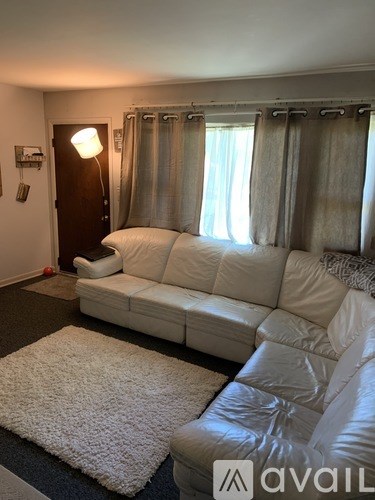 A white leather couch in a living room with a rug and a lamp.