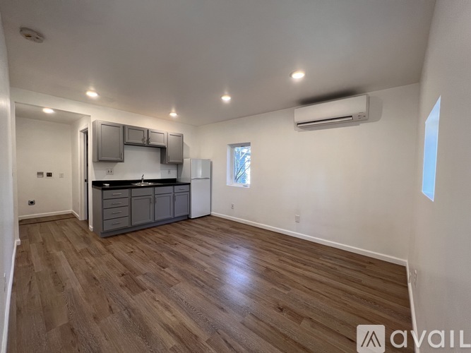 A spacious room with wooden flooring and a kitchen area with a refrigerator, microwave, and cabinets.
