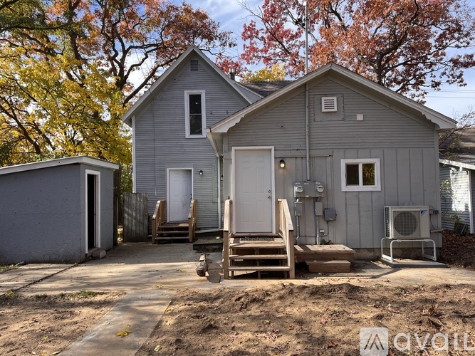 A grey house with a white door and windows is surrounded by trees.