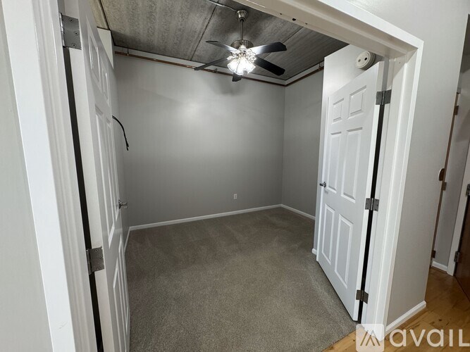 A small, empty room with a ceiling fan and carpeted floor.