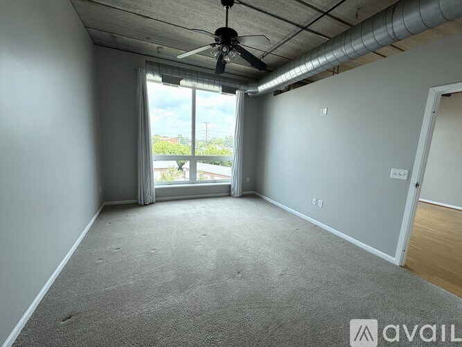 A room with a carpeted floor, a ceiling fan, and a sliding glass door leading to a balcony.