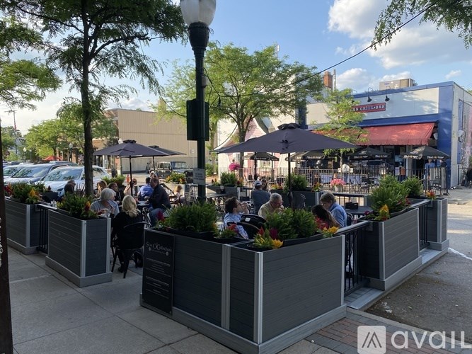 A group of people are sitting at tables under umbrellas on a sunny day.